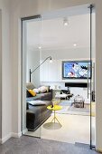 Blick durch offene Glastür auf gelben Beistelltisch und braunes Ledersofa, im Hintergrund Flachbild Fernseher an Wand