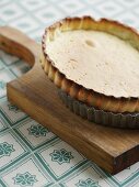 A baked shortcrust pastry base in a tart dish on a wooden board