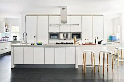 White, designer kitchen with bar stools at counter in open-plan interior