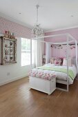 Rosa getöntes Mädchenzimmer mit Doppelbett und weißem Himmelgestell, davor Truhe mit Sitzpolster als Bettbank, auf rustikalem Dielenboden