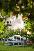 Garden bench in front of roses and petunias in flowerbed