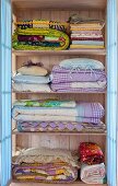 Folded bedclothes in a pastel blue laundry cupboard