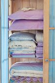 Stacks of pastel-blue bedclothes and pillows in a light wooden cupboard