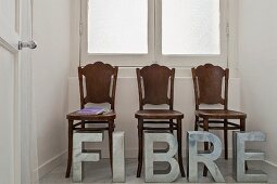 Three old wooden chairs in a window alcove, silver metal letters in front of them