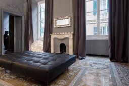 Black leather ottoman on terrazzo floor in front of open fireplace in elegant old building