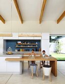 Esstisch aus Massivholz als Erweiterung der Theke in offener Küche, zwei Mädchen am Tisch