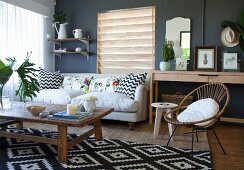 Rustic wooden coffee table on black and white patterned rug and sofa with scatter cushions in interior with dark wall