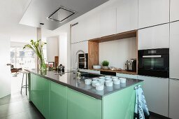 A white fitted kitchen with wooden details and an extractor hood above a mint-coloured kitchen island