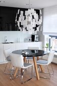 Esstisch mit schwarzer, runder Platte und weiße Stühle unter Designer-Zetteleuchte in offener Küche