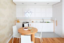 Round wooden table and white chairs in front of kitchen counter with white wall units