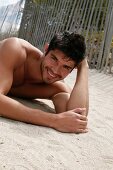 A young, topless man lying in the sand