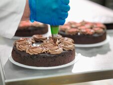 A baker decorating cake with chocolate cream in a cake factory