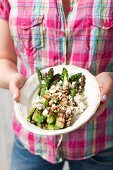 A woman holding a plate of grilled green asparagus with feta cheese and balsamic vinegar