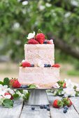 A two-tier cream cake decorated with berries on a table outside