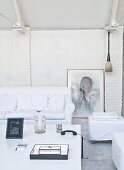 Sofa and pouffe with white loose covers around coffee table in living area with whitewashed brick wall