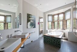 Washstand with twin sinks and modern, free-standing bathtub in window bay of large bathroom