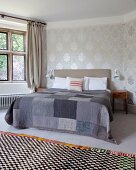 Checked rug in front of double bed with patchwork blanket in various shades of grey in traditional bedroom