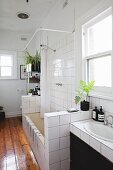 Washstand and bathtub with half-height, tiles partition walls and varnished wooden floor in bathroom of period apartment
