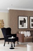 Black wing-back chair and side table next to sofa against wall with brown structured wallpaper