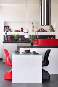 Red and black shell chairs at white table in open-plan designer kitchen