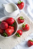 Fresh strawberries in a bowl with a jug of cream on a linen cloth