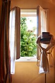 Hat and draped scarves on old tailors' dummy in front of open window