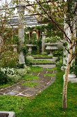 Antique columns lining path and steps leading to stone bench in seating area with planted urn