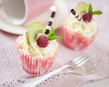Cupcakes decorated with white chocolate cream, kiwis, raspberries and chocolate cigars
