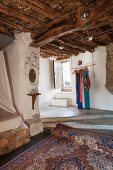 Oriental rug below concrete platform leading to staircase in rustic country house with wood-beamed ceiling