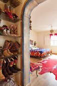 Cowboy boots on shoe rack an view into ethnic-style bedroom through painted archway