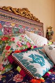 Bed headboard covered in colourful fabric and ethnic-style scatter cushions