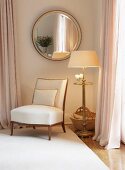 Upholstered chair below round mirror on wall in corner of elegant bedroom