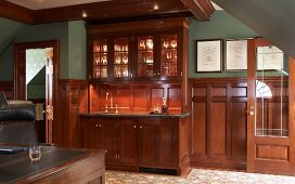 Smoking room with panelled wainscoting and glasses under spotlights in elegant, glass-fronted cabinet