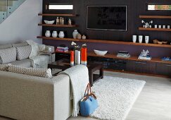 Elegant lounge area with pale sofa set opposite wall painted dark purple with wooden shelves and integrated flatscreen TV