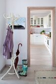 Coat stand and wellingtons in hall next to doorway leading into white fitted kitchen