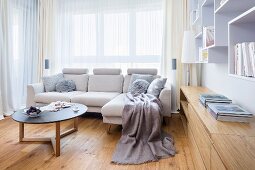 Pale couch and coffee table in front of window next to pale wood, fitted sideboard