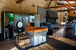 Old, country-house-style kitchen counter next to wooden crate on industrial scales; stainless steel fridges in background