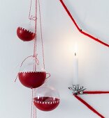 In rote Farbe getauchte Weihnachtskugeln aus Glas mit Kreuzmuster hängen neben brennender Kerze