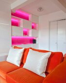 Fitted cabinets with shelf compartments illuminated bright pink behind orange sofa in white interior