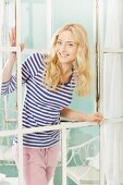 Junge blonde Frau in blau-weiss gestreiftem Shirt lehnt sich aus Vintage Sprossenfenster