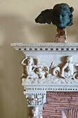 Detail of antique mantelpiece with relief carvings of figures and metal head on plinth