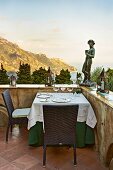 Sculpture on terrace parapet wall, table set for two and coastal landscape in background