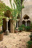 Courtyard with potted plants on terracotta floor and climber-covered arcades at Villa Cimbrone in Italy