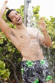 Mann in Badeshorts unter Dusche im Freien