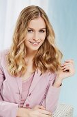 A portrait of a blonde woman wearing a dusky pink blouse and a blazer