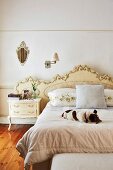Dog lying on double bed with pretty gilt headboard, Rococo-style bedside cabinet and vintage sconce lamp