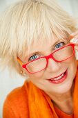 An older woman wearing an orange jumper and scarf and a pair of red glasses