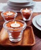 Glass tealight holders filled with red lentils and lit candles