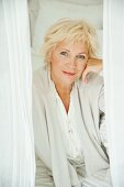 An older woman wearing white pyjamas and a cardigan sitting on a bed