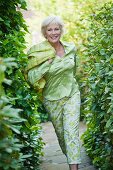 An older woman wearing a light green blouse and green-and-white trousers running in a garden